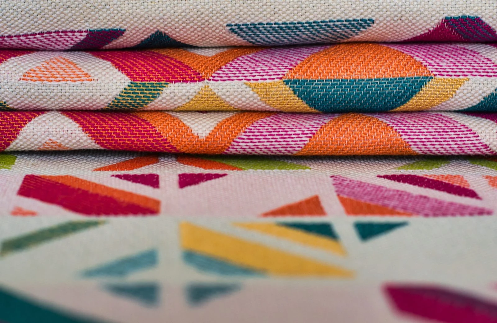 Folded Mexican woven textiles with magenta, orange, teal and yellow geometric patterns