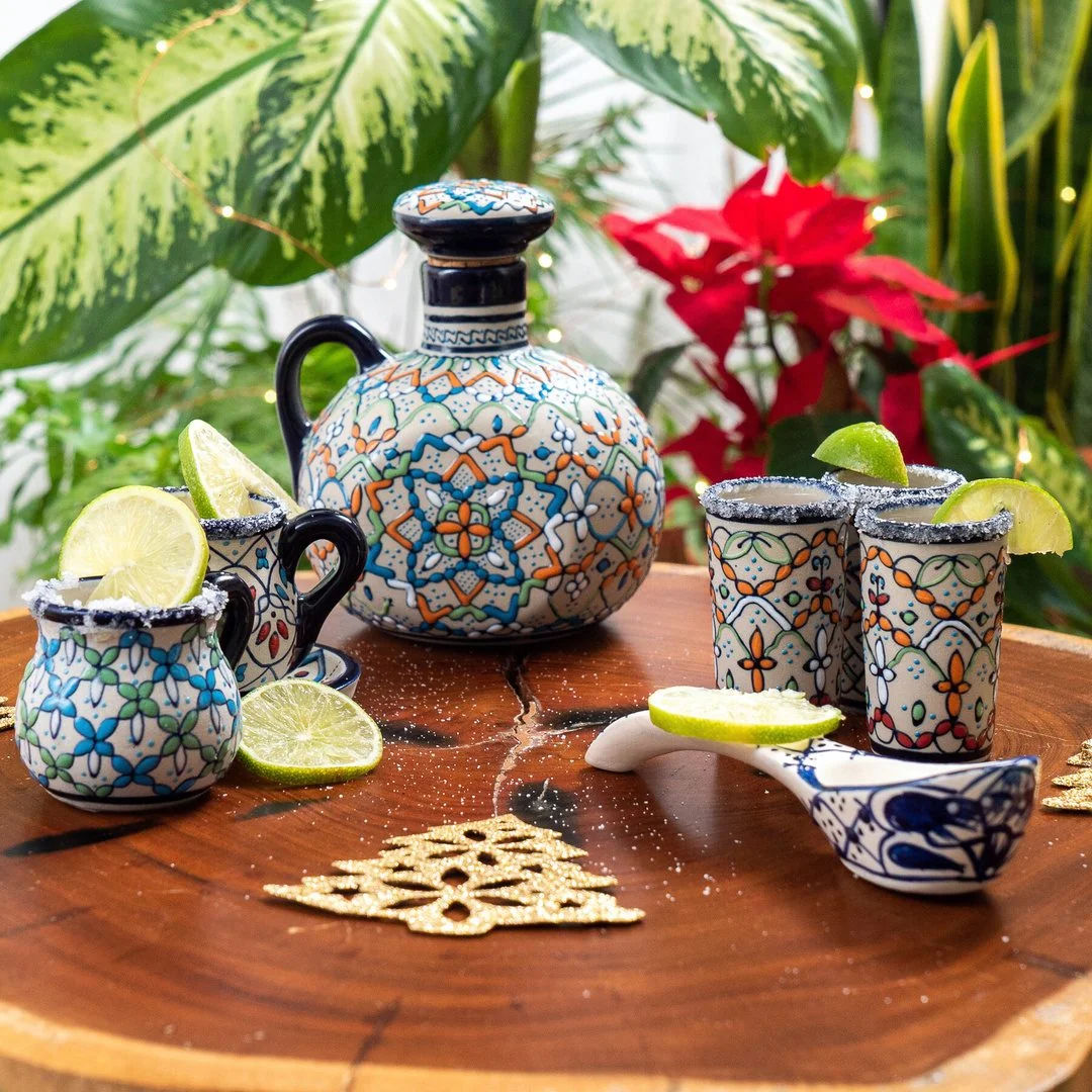 Colorfully painted Mexican ceramic pitcher, cups and small bowls on a table with lime and flowers
